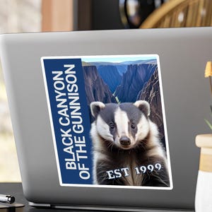 Puede incluir: Adhesivo con un tejón sobre un paisaje de cañón. El adhesivo incluye el texto "BLACK CANYON OF THE GUNNISON" y "EST 1999" en blanco sobre un fondo azul.