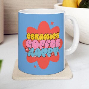 May include: A white ceramic mug with a blue background and a red, pink and yellow graphic that says "ceramics coffee happy".