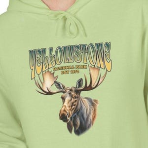Könnte beinhalten: Hellgrüner Kapuzenpullover mit einem Elch-Motiv und dem Text "Yellowstone National Park Est 1872". Der Hoodie hat eine Kängurutasche und eine Kapuze mit Kordelzug.