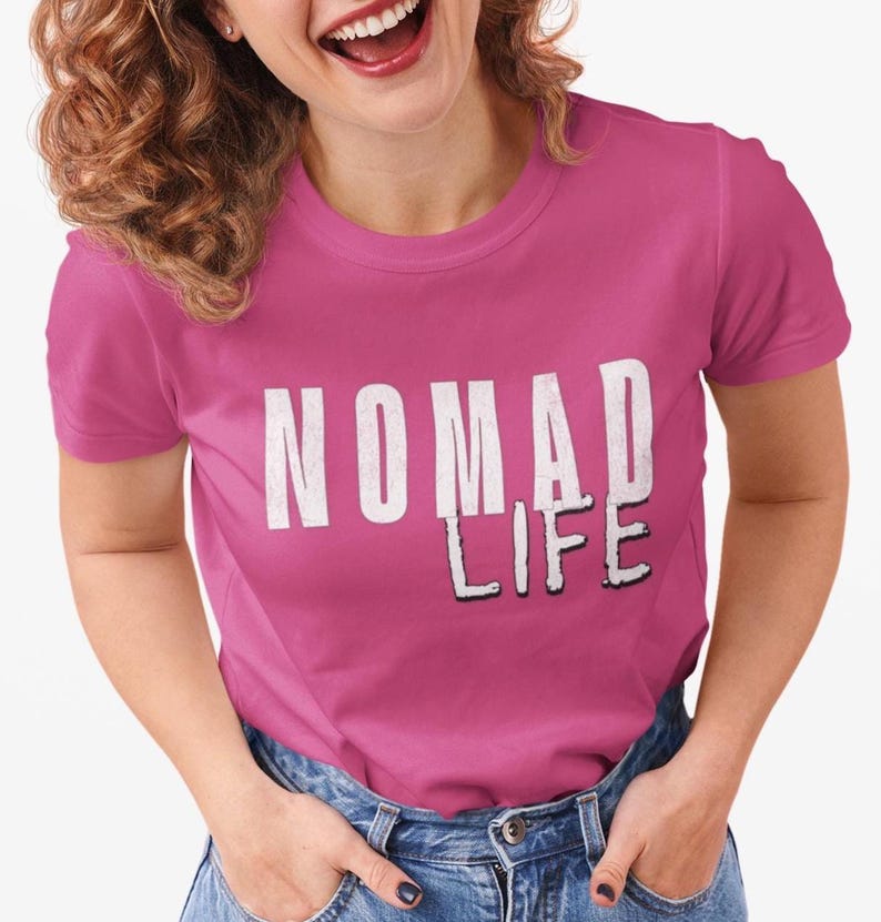 May include: A magenta t-shirt with the words "NOMAD LIFE" printed in white, with a black shadow effect. The shirt is being worn with blue jeans.