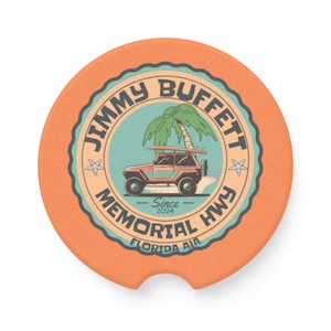 May include: Orange car coaster with a circular design featuring the text "JIMMY BUFFETT MEMORIAL HWY FLORIDA AIA" and a graphic of a jeep with a surfboard in front of a palm tree. The coaster has a small notch for easy removal.