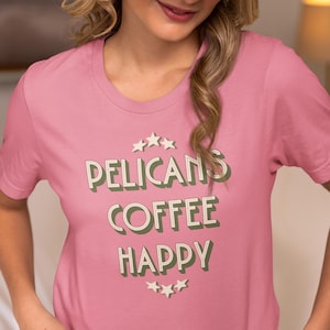 May include: A pink t-shirt with a green graphic that says "Pelicans Coffee Happy" with stars above and below the text.