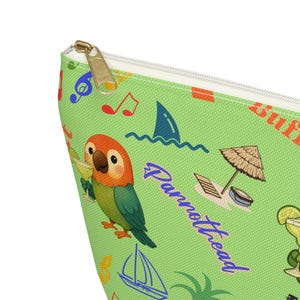 Pode incluir: Uma bolsa verde com zíper com tema tropical. Apresenta um papagaio de desenho animado segurando uma bebida, notas musicais, uma barbatana de tubarão e a palavra "Parrothead" em escrita azul. A bolsa tem um zíper dourado.