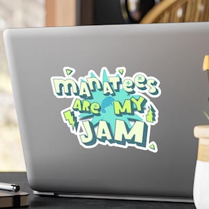 Peut inclure: Autocollant sur un ordinateur portable avec le texte "Manatees are my jam" dans une police ludique. Le texte est souligné en blanc avec une palette de couleurs vert clair et bleu, et un fond en forme d'explosion de dessin animé.