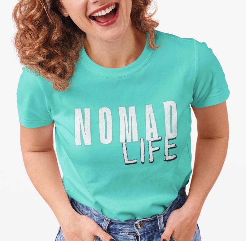 May include: A turquoise crew neck t-shirt with the words "NOMAD LIFE" printed in white. The text has a shadow effect, adding depth to the design. The shirt is made of a soft material.