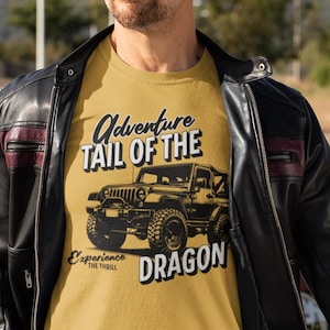 May include: Mustard yellow t-shirt with a black graphic of a Jeep and the words "Adventure Tail of the Dragon". The text "Experience the Thrill" is also printed on the shirt. The person is wearing a black leather jacket.