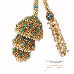 May include: A gold and turquoise beaded lariat necklace with a jhumka design. The necklace features a series of cascading, round beads with a turquoise accent. The lariat is finished with a tassel of white pearls.