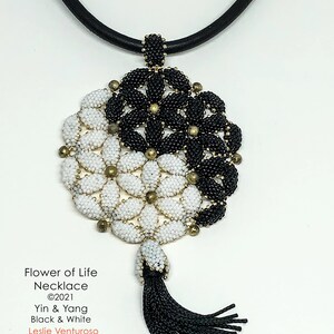 May include: A black and white beaded necklace with a flower of life pendant and a black tassel. The pendant is made of small beads and features a yin yang design. The necklace is made of black leather cord.