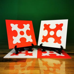 Peut inclure: Deux carreaux de céramique avec un motif géométrique blanc sur fond rouge et blanc. Les carreaux sont exposés sur des supports noirs.