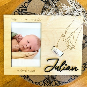 Può includere: Una cornice per foto in legno con un nome inciso in nero "Julian" e una piccola foto di un neonato. La cornice include anche i dettagli di nascita del bambino: 3742g, 52 cm, 16:26 Uhr, 09. ottobre 2023.