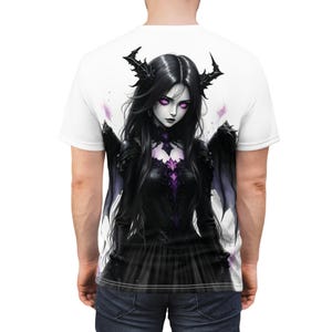 Könnte beinhalten: Ein weißes T-Shirt mit einer schwarzen und violetten Illustration einer Frau mit Hörnern und Flügeln. Die Frau trägt ein schwarzes Kleid mit einem Spitzenoberteil.