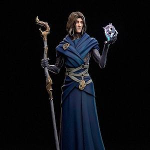 May include: A detailed figurine of a character in a flowing blue robe, holding a staff and a glowing orb. The staff has gold accents, and the character has long brown hair and a serious expression. The background is black.