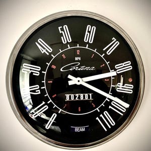 Könnte beinhalten: Ein schwarzer und silberner Cortina-Tachometer mit weißen Ziffern, die die Geschwindigkeit in MPH anzeigen. Der Tachometer zeigt 802801 an und hat das Wort "BEAM" unten. Das Zifferblatt ist von einem silbernen Metallrand umgeben.