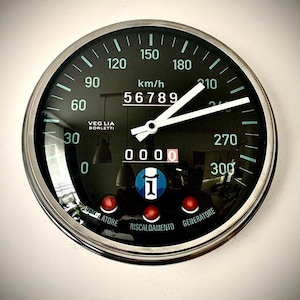 Könnte beinhalten: Ein schwarzer und silberner Tachometer mit weißen Zeigern und grünen Markierungen. Der Tachometer zeigt 56789 km/h an. Das Messgerät trägt die Aufschrift "VEGLIA BORLETTI" und "km/h". Unten befinden sich drei rote Lichter.