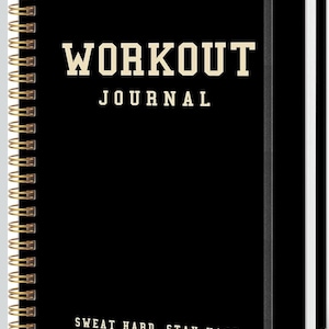 May include: Black spiral-bound workout journal with gold accents. The cover features the words "WORKOUT JOURNAL" in a bold, serif font. Below the title is the phrase "SWEAT HARD, STAY HARD" in a similar font. The journal has a gold spiral binding.