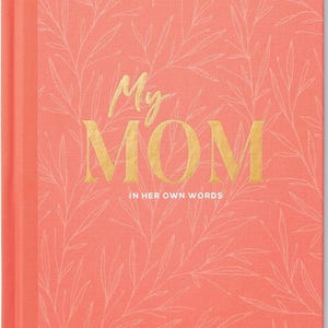 May include: A coral-colored journal with the words "My MOM" in gold lettering. The cover features a delicate, light-colored leaf pattern. The text "IN HER OWN WORDS" is below the main text.