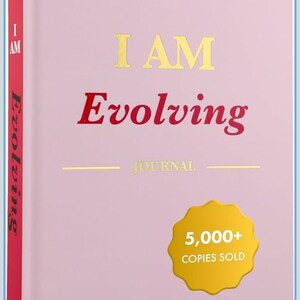 May include: A pink journal with the words "I AM Evolving" in gold and red lettering. The journal includes the word "JOURNAL" and a gold seal that says "5,000+ COPIES SOLD". The journal's cover also includes the text "Set Goals, Embrace Gratitude, Cultivate Habits, Achieve Inner Peace."
