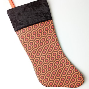 May include: A Christmas stocking with a black velvet cuff and a red and orange geometric pattern. The pattern is reminiscent of the Overlook Hotel carpet from the movie "The Shining."