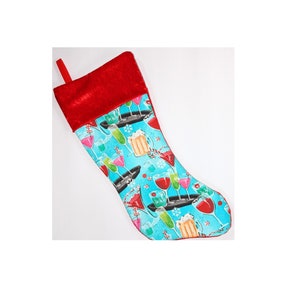 Puede incluir: Una media de Navidad roja y azul con un diseño festivo de cócteles y bebidas sobre un fondo azul.