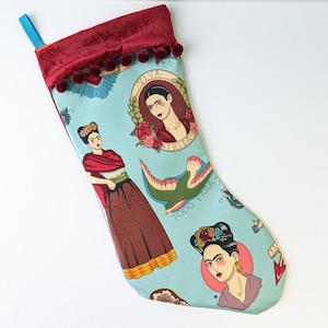 Puede incluir: Una media de Navidad azul y roja con un diseño festivo que presenta a Frida Kahlo, un pájaro y el texto "Viva Frida" y "Todo Para".