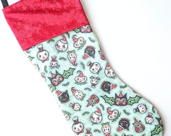 Puede incluir: Una media de Navidad de terciopelo rojo con una tela verde y blanca con un patrón repetitivo de varios personajes navideños, incluyendo muñecos de nieve, murciélagos y búhos.