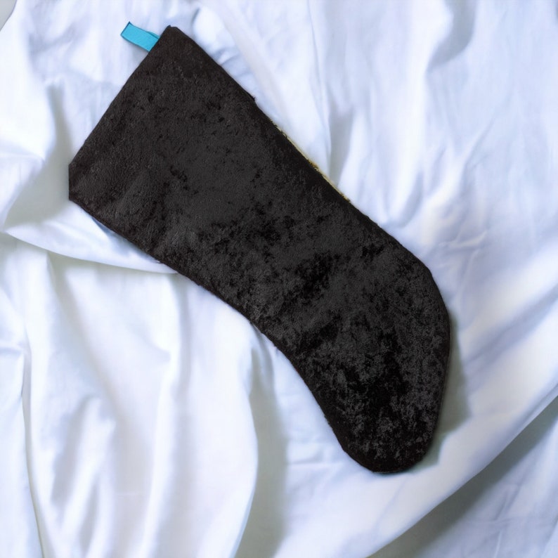 May include: A black velvet stocking with a blue ribbon at the top, lying on a white sheet.