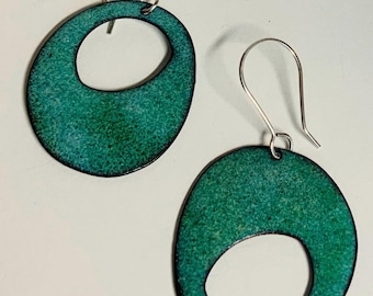 May include: A pair of teal green earrings with a circle cut out of the center. The earrings are made of metal and have a textured finish.