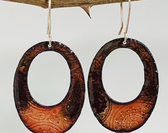 May include: Oval-shaped earrings with a textured, earthy design. The earrings feature a dark brown outer edge that fades into a lighter orange-brown center with a detailed pattern. The earrings hang from silver-colored hooks.