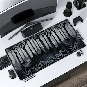 May include: A black and white illustrated mousepad featuring a dark forest scene with trees and a winding path. The mousepad is on a white desk with other office supplies.