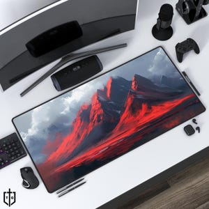 May include: A large red and black mountain landscape printed on a black gaming mouse mat. The mouse mat is on a white surface with a computer monitor, a speaker, a microphone, a controller, and a pen.