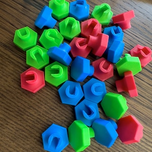 May include: A collection of colorful hexagonal plastic pieces with a variety of colors including blue, green, and red. The pieces have a small hole in the center.