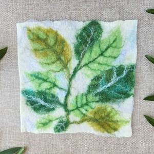 May include: A white felt piece with a green and yellow leaf design. The leaves are detailed with veins and have a textured look.
