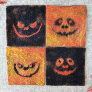 May include: Four felt squares with different Halloween-themed faces. Each square is a different color combination of black, orange, and yellow.