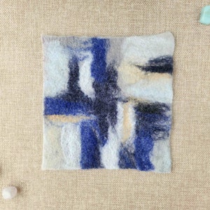 May include: A square piece of felted wool with abstract designs in shades of blue, white, and black.