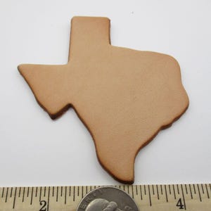 May include: A tan leather cutout in the shape of the state of Texas. The cutout is approximately 3 inches long. The edges are a darker brown. A coin is at the bottom of the image.