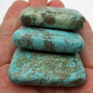 May include: Three polished, rectangular turquoise stones stacked vertically. Each stone features a distinct natural matrix pattern with varying shades of bright cyan, light blue, and earthy brown inclusions across their smooth, flat surfaces.