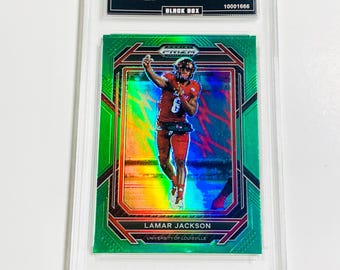 May include: A graded Green Prizm Lamar Jackson trading card from the 2023 Prizm Draft Picks set. The card features a photo of Lamar Jackson in a red uniform. The card is encased in a protective holder.