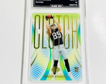 May include: A trading card encased in a clear plastic holder. The card features an image of a football player in a Raiders uniform catching a ball. The word "CLUTCH" is prominently displayed. The card is labeled "2024 ILLUSIONS BROCK BOWERS".