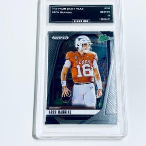 Puede incluir: Una tarjeta de fútbol de Arch Manning calificada de la serie 2025 Prizm Draft Picks. La tarjeta presenta a Manning con su uniforme de los Texas Longhorns, con el número 16. La tarjeta está calificada como GEM MT 10 y está dentro de un soporte protector.