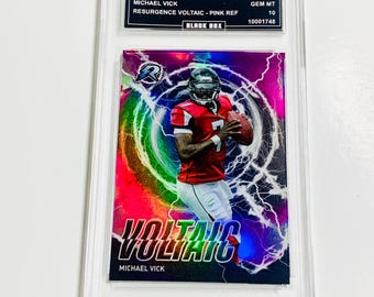 May include: A Michael Vick football trading card in a protective case. The card features a player in a red uniform against a pink and purple background with lightning effects. Text includes "VOLTAIC" and "2023 TOPPS COMPOSITE".