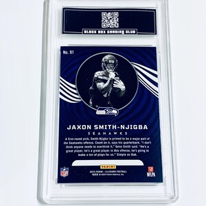 May include: A Jaxon Smith-Njigba Seahawks football card, graded by Black Box Grading Club, encased in a clear protective holder. The card features a player image and text, including "2023 Panini - Illusions Football."