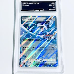 Puede incluir: Una carta de Pokémon calificada con Lugia ex del conjunto Prismatic Evolutions. La carta tiene un diseño holográfico con colores azules y blancos. La carta está encerrada en una funda protectora transparente con una etiqueta negra que incluye el texto "BLACK BOX".