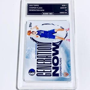Puede incluir: Una tarjeta de baloncesto Cooper Flagg Generation Now Topps 2025 calificada. La tarjeta presenta a un jugador con uniforme azul, en el aire con un bal&oacute;n de baloncesto. La tarjeta est&aacute; dentro de un soporte protector transparente con una etiqueta negra.