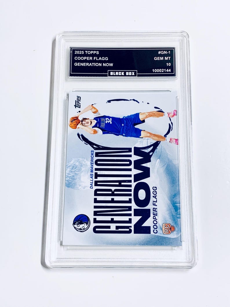 Puede incluir: Una tarjeta de baloncesto Cooper Flagg Generation Now Topps 2025 calificada. La tarjeta presenta a un jugador con uniforme azul, en el aire con un bal&oacute;n de baloncesto. La tarjeta est&aacute; dentro de un soporte protector transparente con una etiqueta negra.