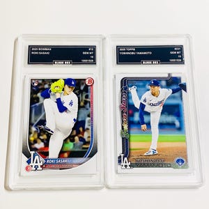 May include: Two baseball trading cards in protective cases. One card features Roki Sasaki of the Los Angeles Dodgers, the other Yoshinobu Yamamoto. Both cards are graded GEM MT 10 by Black Box.