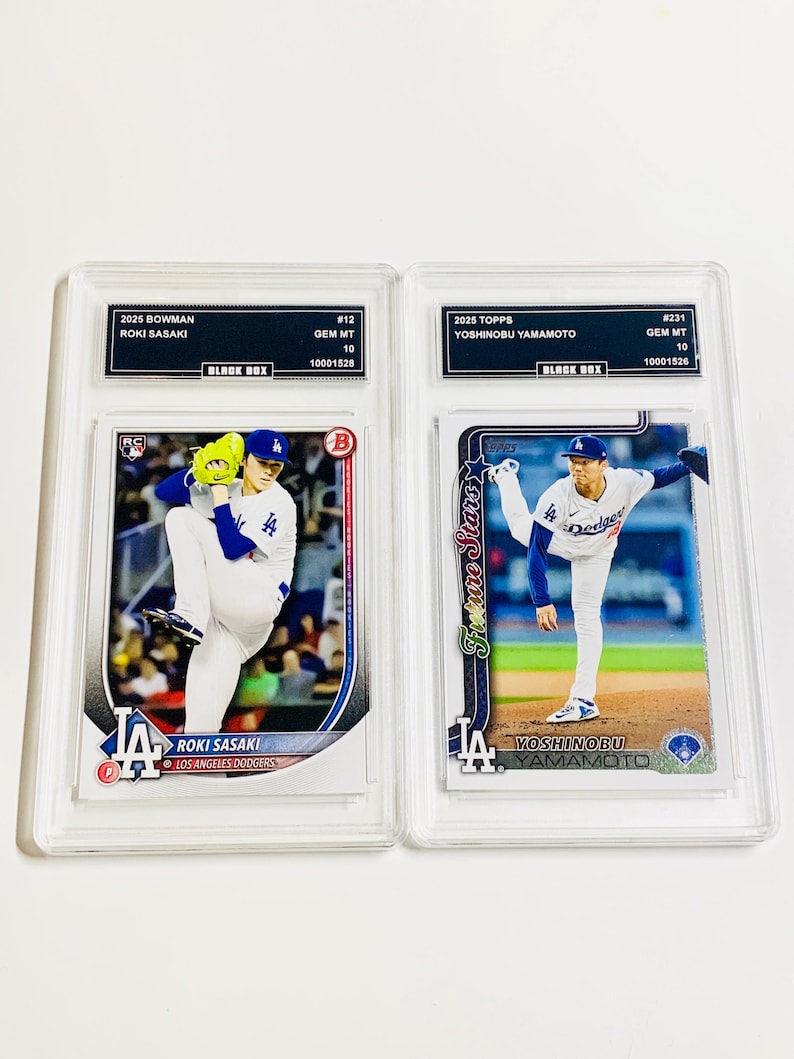 May include: Two baseball trading cards in protective cases. One card features Roki Sasaki of the Los Angeles Dodgers, the other Yoshinobu Yamamoto. Both cards are graded GEM MT 10 by Black Box.