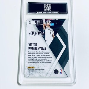 K&ouml;nnte beinhalten: Eine bewertete Basketballkarte mit Victor Wembanyama von den San Antonio Spurs. Die Karte ist in einem transparenten Kunststoffhalter mit dem Text "BLACK BOX GRADING CLUB" oben eingeschlossen. Die Karte hat unten den Text "PANINI".