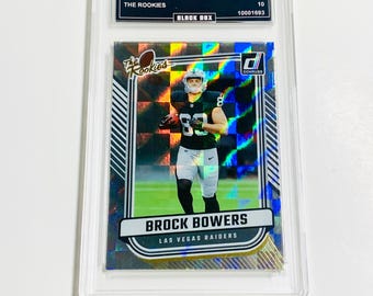 May include: A 2024 Donruss Brock Bowers football trading card, graded GEM MT 10, encased in a protective holder. The card features a photo of Brock Bowers in a Las Vegas Raiders uniform. The card has the text "The Rookies" and "Black Box".