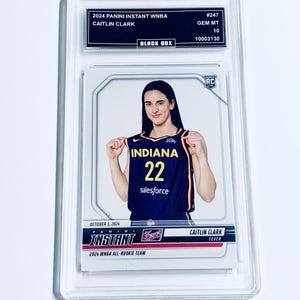 May include: A Caitlin Clark Panini Instant WNBA trading card, in a protective case. The card shows Clark in an Indiana Fever uniform, with the number 22. The card is graded GEM MT 10.