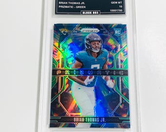 May include: A 2024 Prizm Brian Thomas Jr. football trading card, graded GEM MT 10, encased in a protective holder. The card features a player in a teal uniform with the text "PRIZMATIC - GREEN" and "BRIAN THOMAS JR."